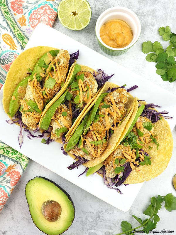 tacos on platter with sauce, avocado, and lime