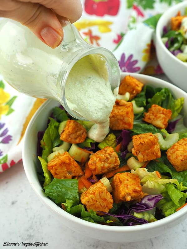 pouring ranch dressing over buffalo tempeh salad