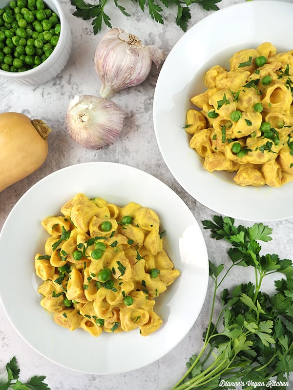 two bowls of Vegan Butternut Squash Mac and Cheese overhead with garlic, peas, and squash