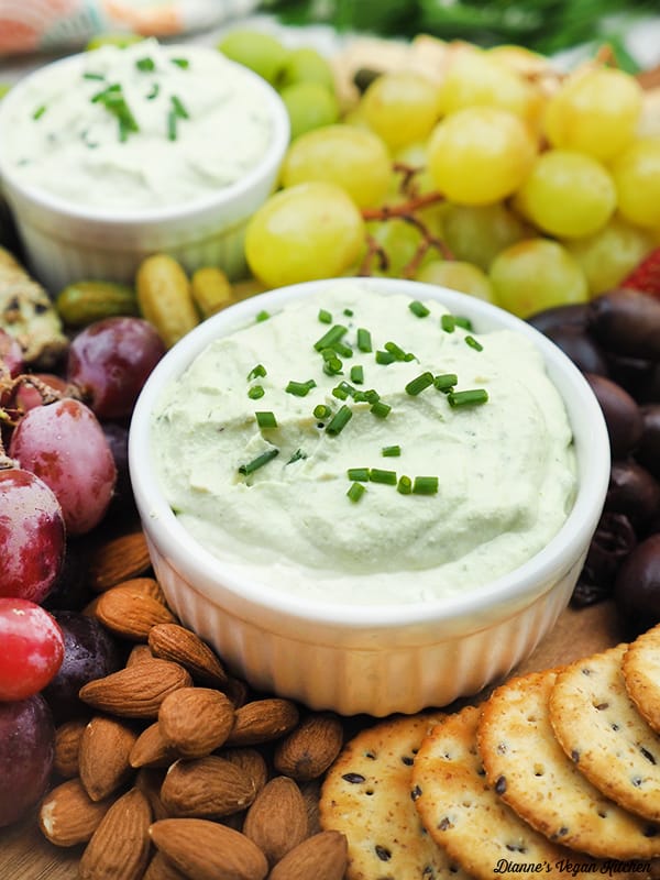 close up of pot of Vegan Garlic and Herb Cheese Spread with nuts, crackers, and grapes