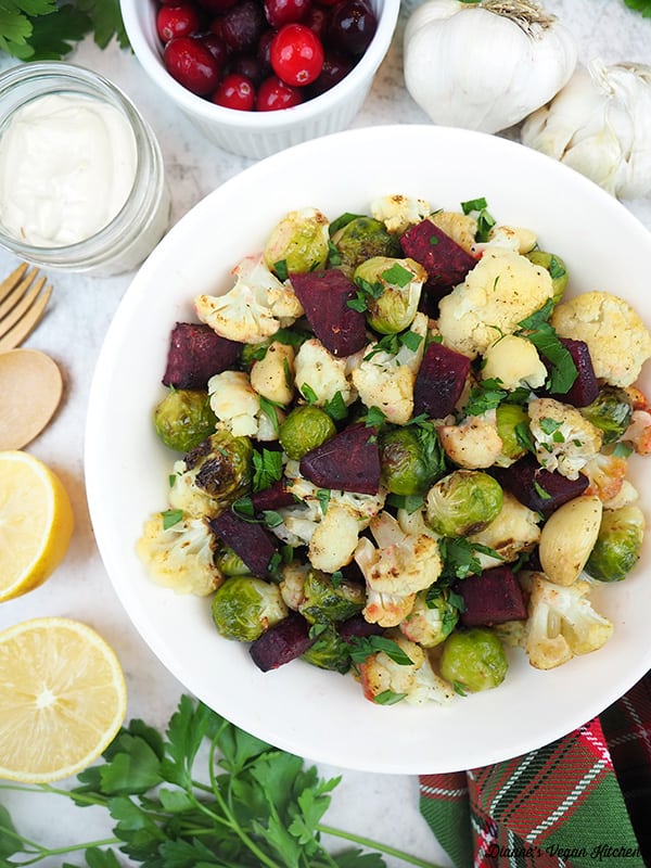 roasted vegetables in bowl with tahini dressing, lemons, and garlic