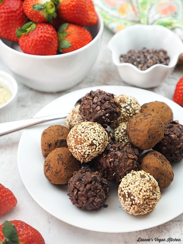 tahini truffles on plate with strawberries, sesame seeds, and cacao nibs