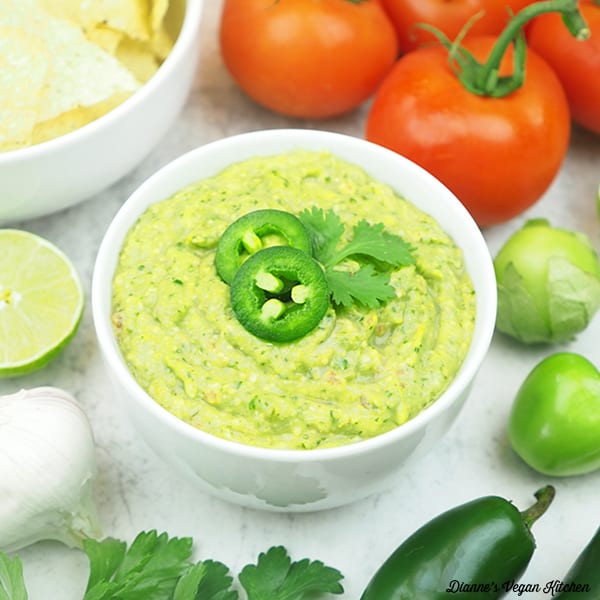 bowl of salsa verde with tomatoes, chips, tomatillos, jalapenos, limes, and cilantro