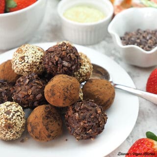 tahini truffles on plate with strawberries, sesame seeds, and cacao nibs