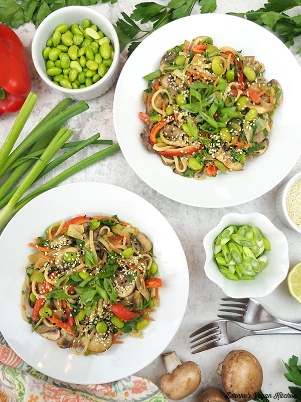 two bowls of stir-fry with edamame, mushrooms, bell pepper, garlic, scallions, and lime