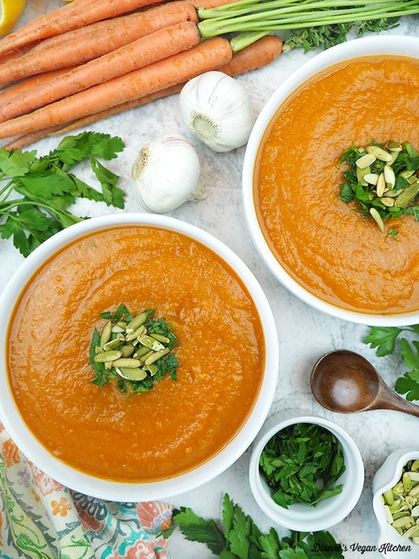 two bowls of Red Lentil and Carrot Soup with carrots, garlic, parsley, and pumpkin seeds