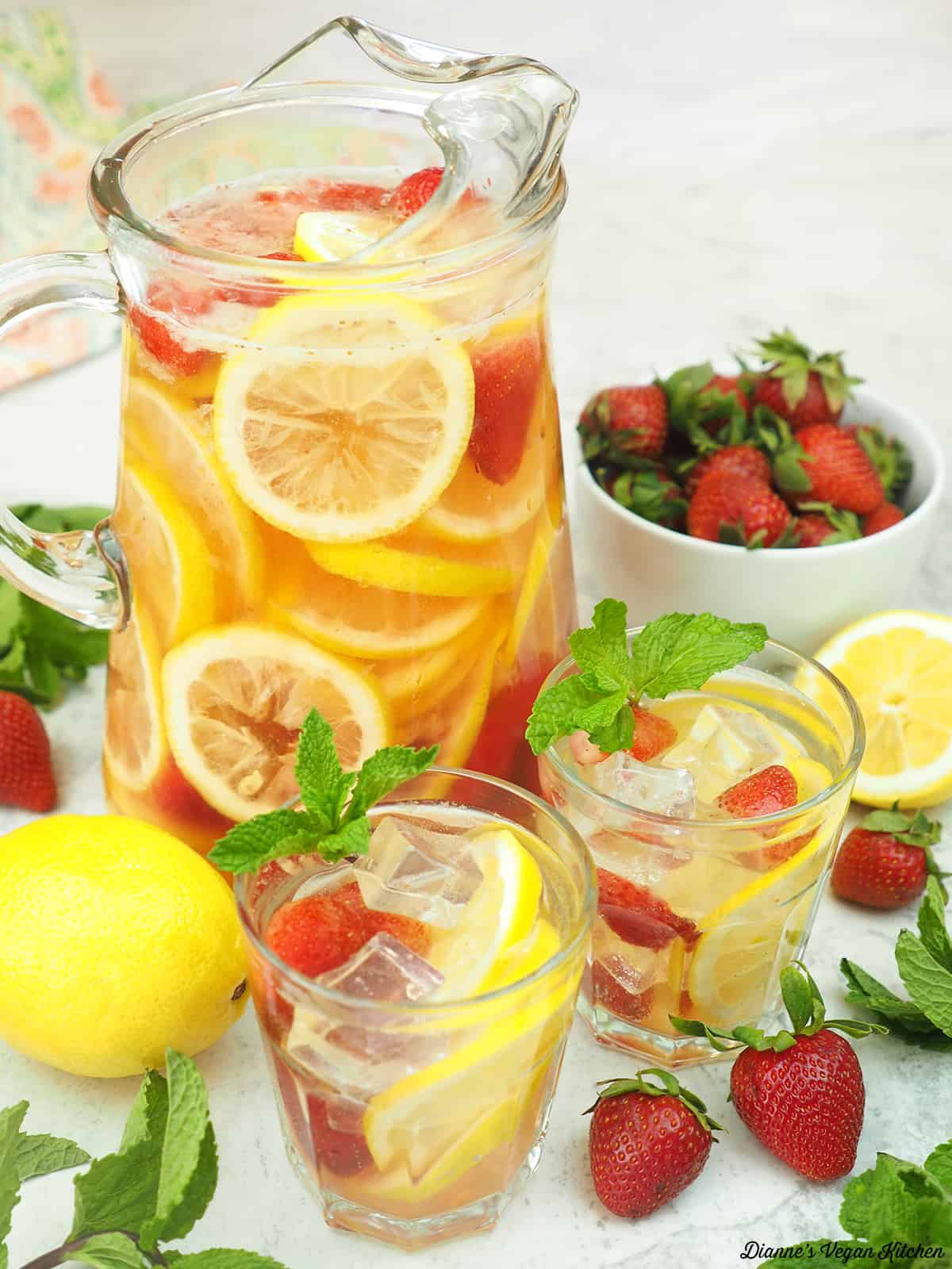 two glasses of white wine sangria with pitcher, lemon, and strawberries