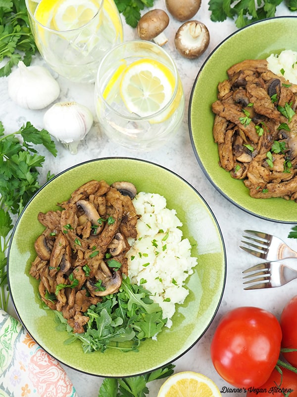 two plates of vegan marsala with lemon water, mushrooms, garlic, forks, and tomatoes