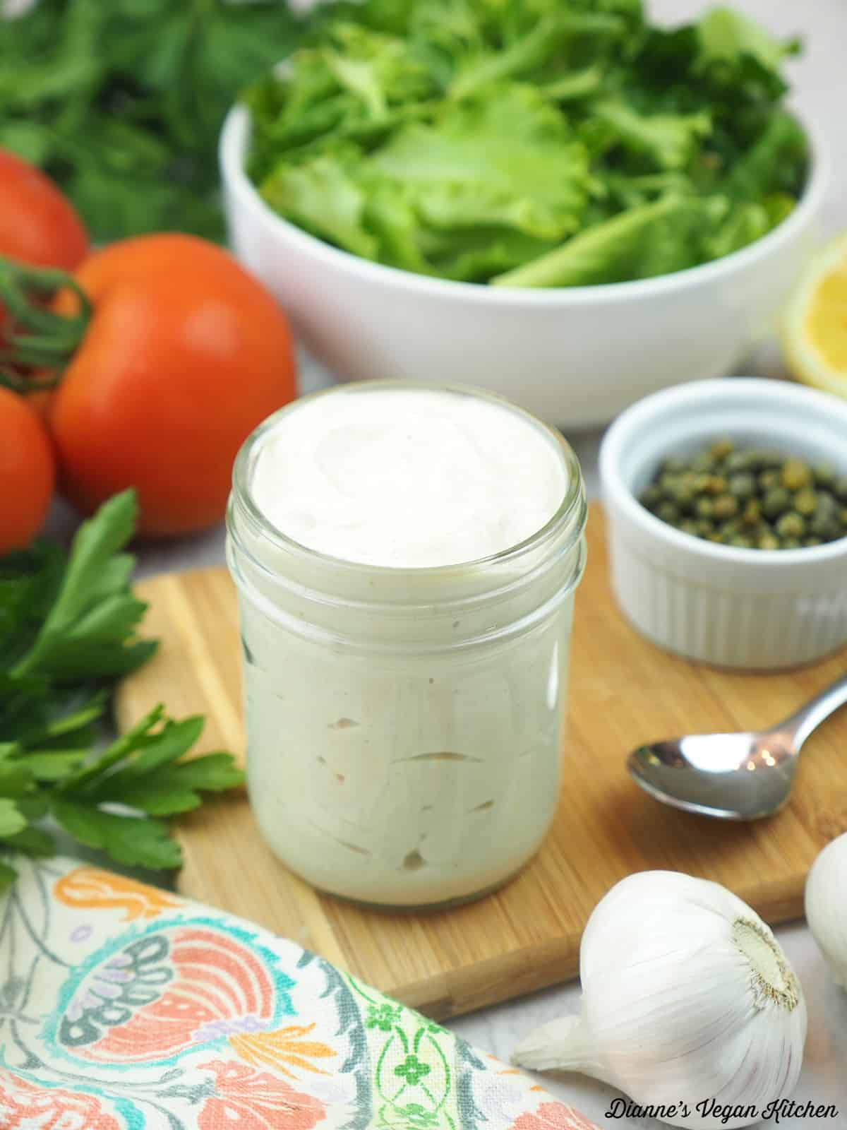 caesar salad dressing with salad, lemon, spoon, capers, and tomatoes