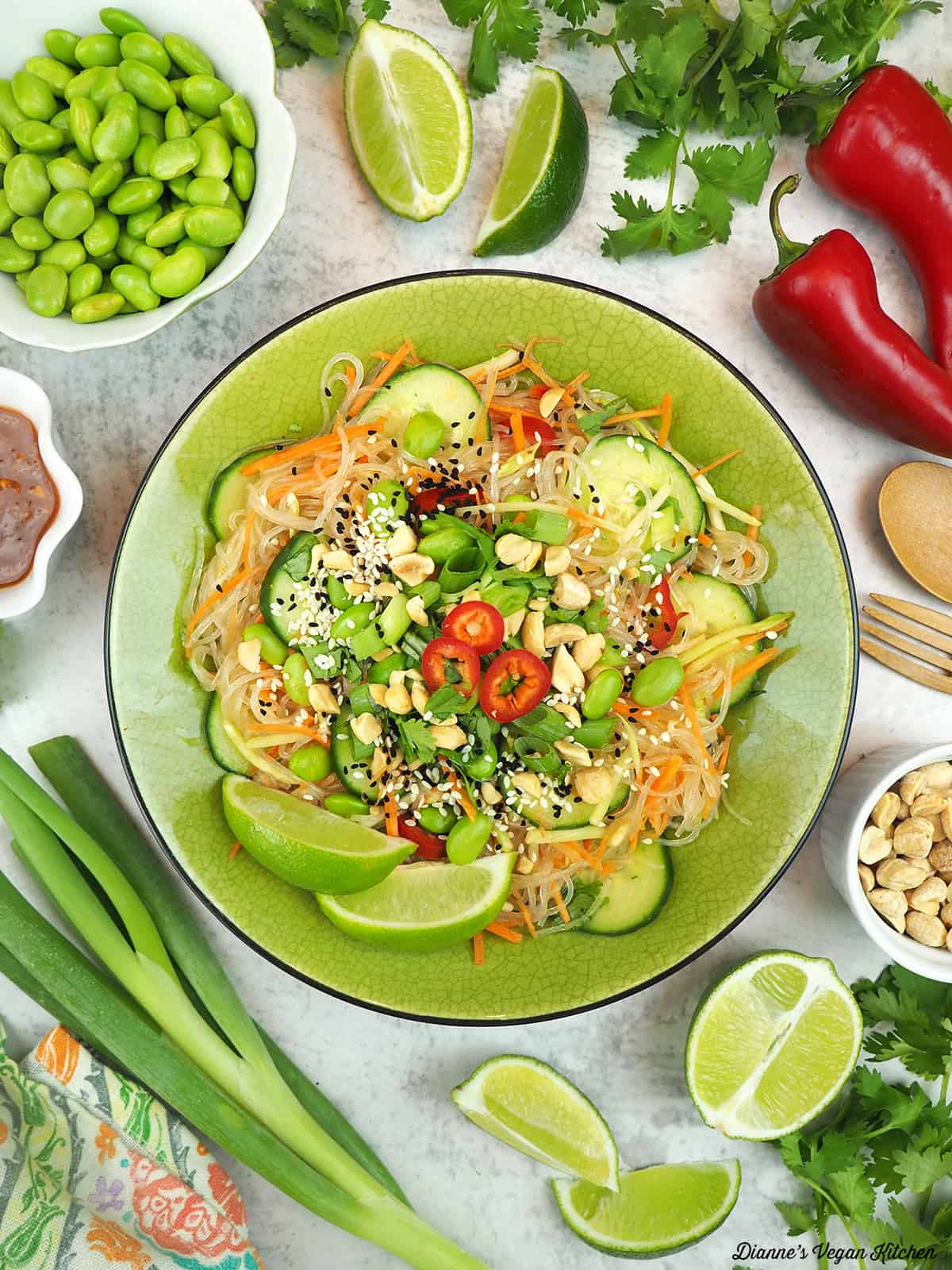 thai noodle salad with fork and spoon, limes, scallions, cilantro, peppers, edamame, and peanuts