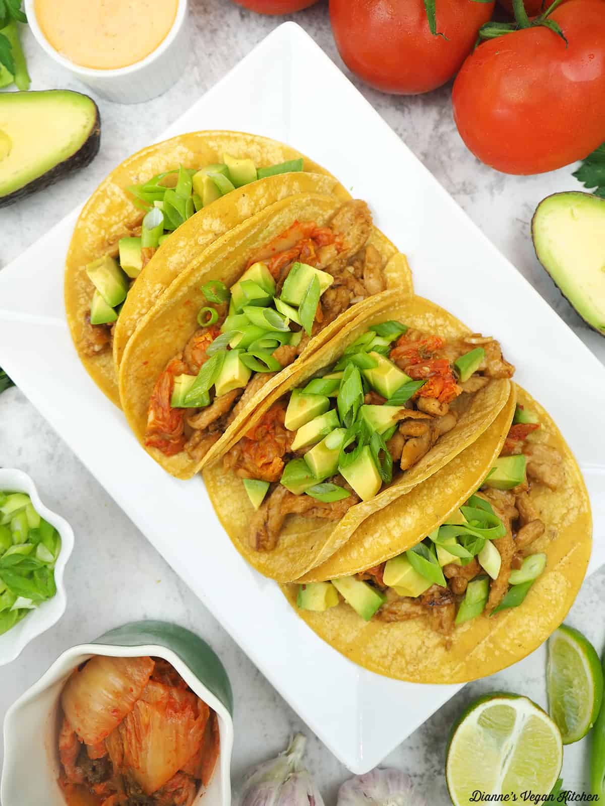 Soy Curl and Kimchi Tacos on platter with tomatoes, scallions, limes, spicy mayo, scallions, garlic, kimchi, and avocado