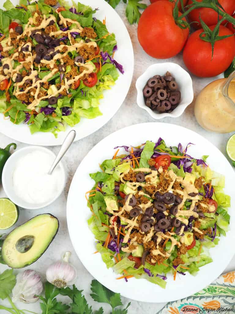 two plates of taco salad with tomatoes, cashew sour cream, chipotle dressing, tomatoes, limes, olives, avocado