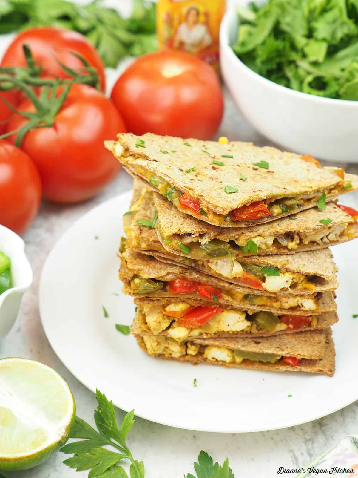 stack of breakfast quesadillas with tomatoes, salad, avocado, and lime