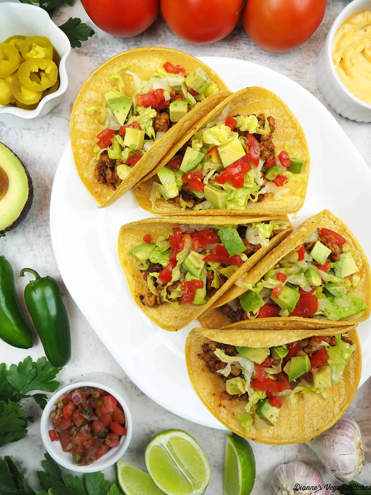 tacos on platter with jalapeños, tomatoes, avocado, salsa, limes, garlic, and cheese sauce