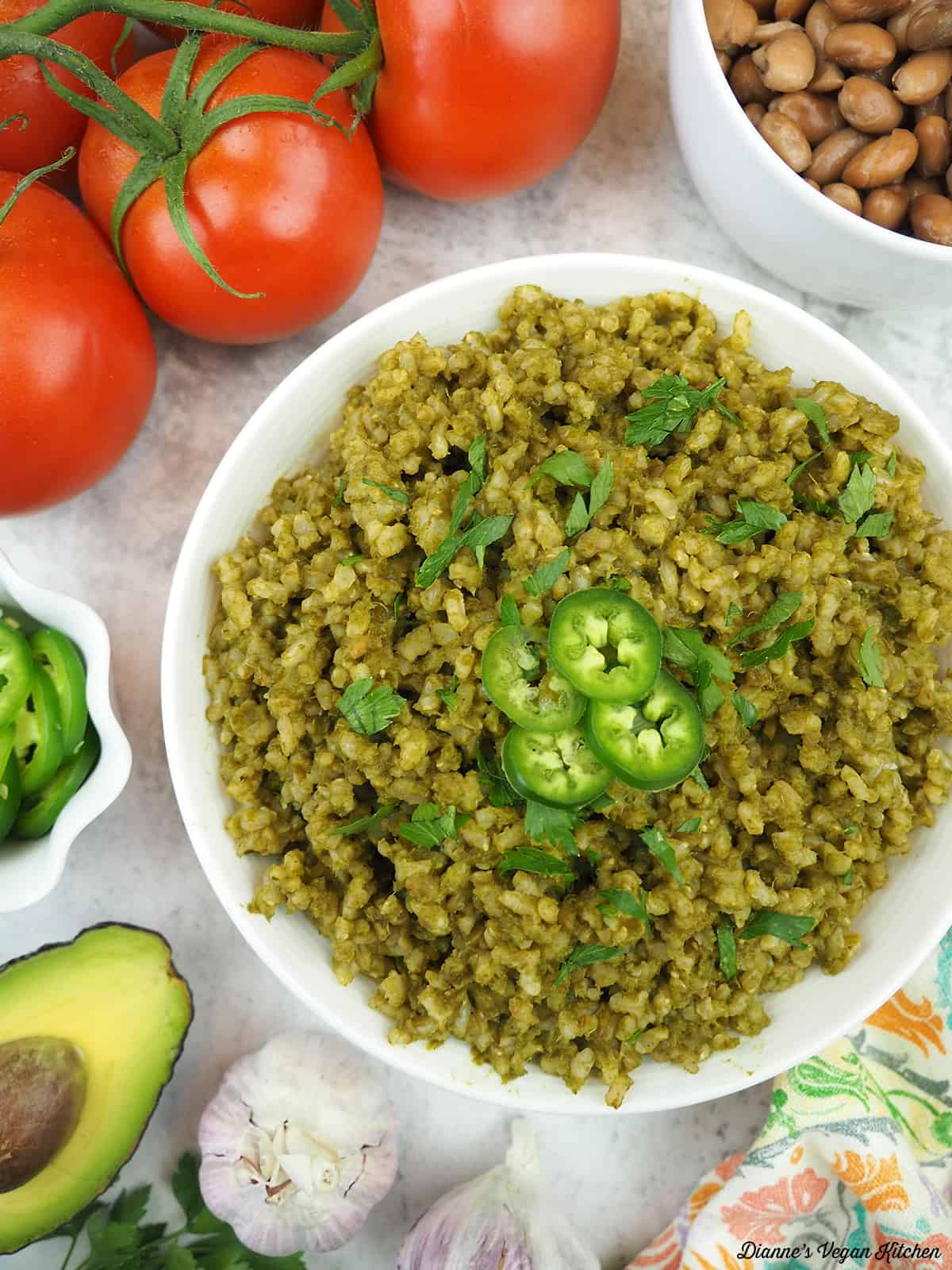 bowl of green rice overhead with beans, tomatoes, garlic, jalapeños and avocado
