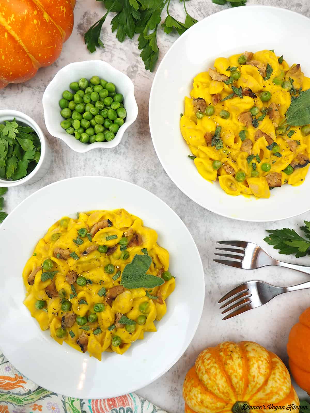 two bowls of pumpkin pasta carbonara with peas, forks, scallions, and pumpkins