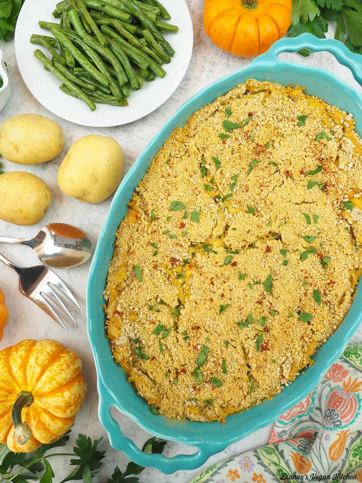 Potatoes Au Gratin in casserole dish with green beans and mini pumpkins