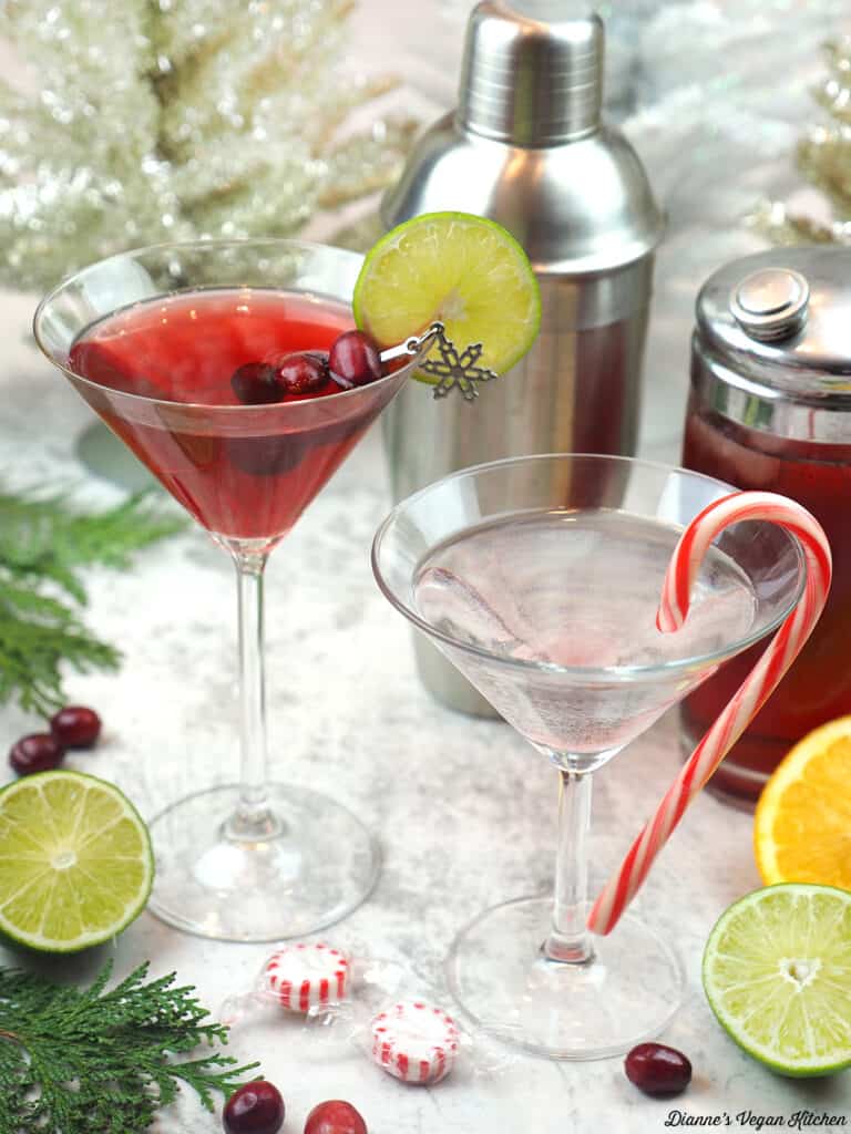 christmas cosmo and candy cane martini with two cocktail shakers, mints, limes, and oranges