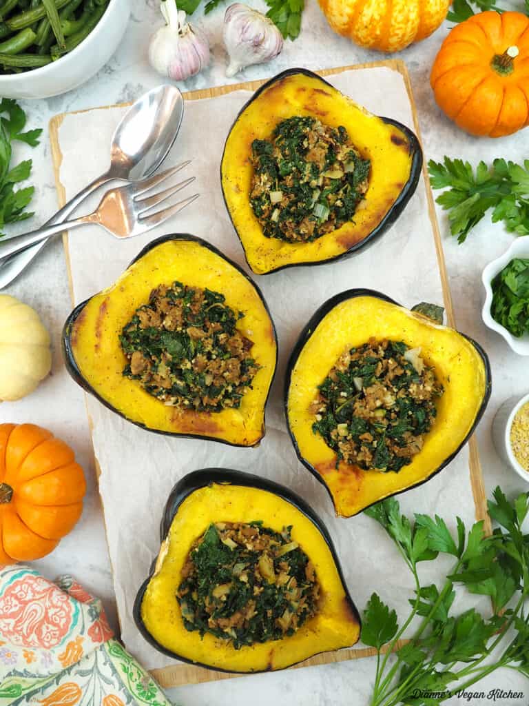 stuffed squash on a cutting board with a fork and spoon. garlic, green beans, mini pumpkins and parsley surround the cutting board