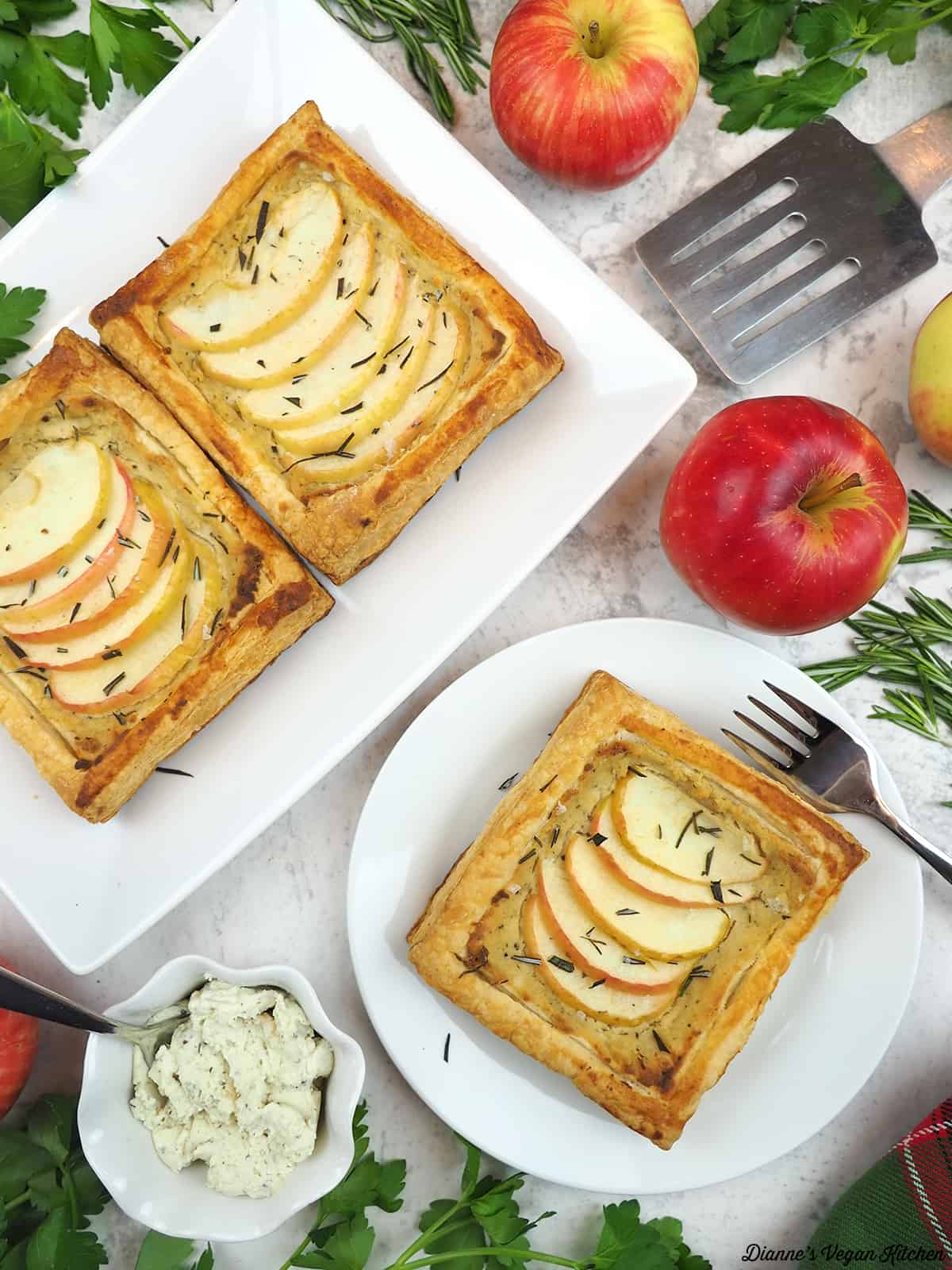 two tarts on a large plate, one tart on a small plate, apples, cheese, and a spatula