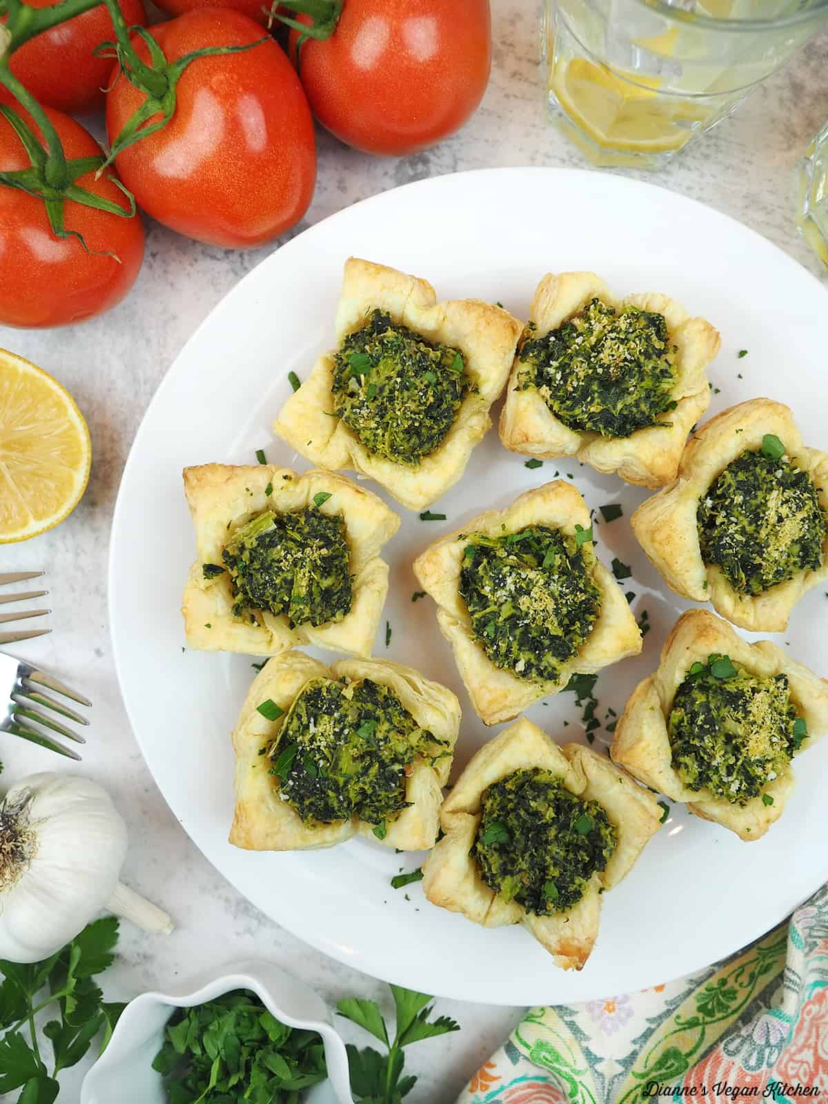 spinach artichoke dip bites overhead with tomatoes, lemon water, garlic, parsley, and forks