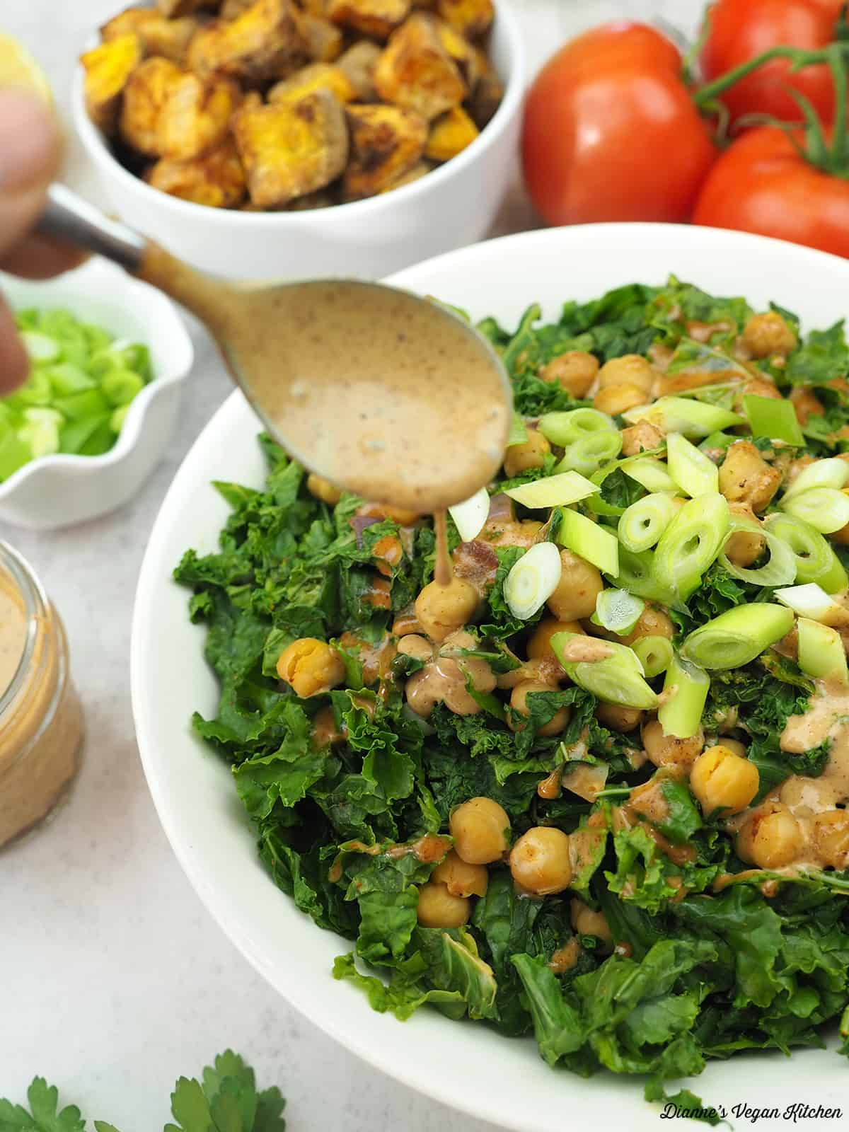 spooning miso peanut drizzle onto kale and chickpeas