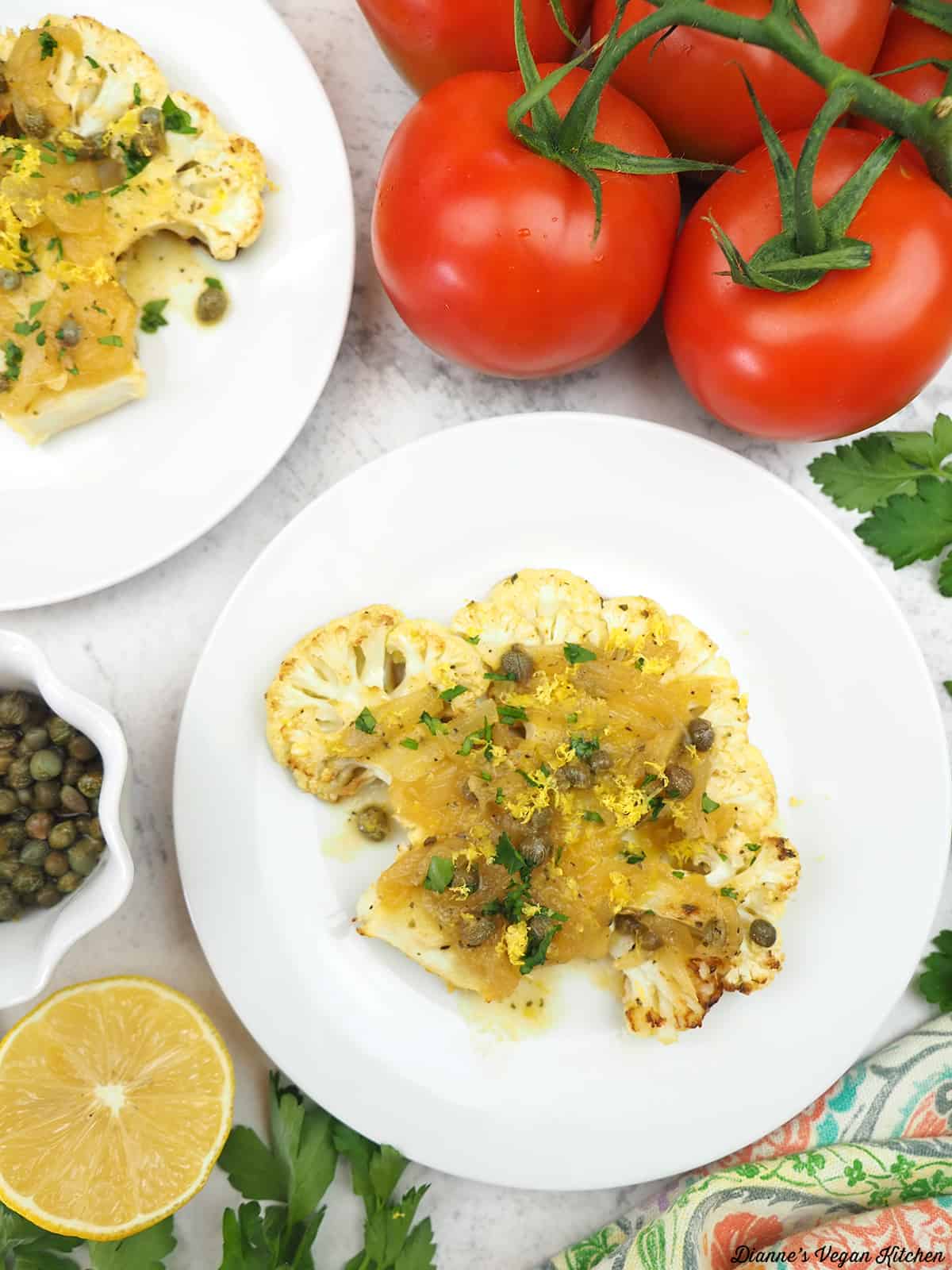 two plates of cauliflower with capers, lemon, and tomatoes