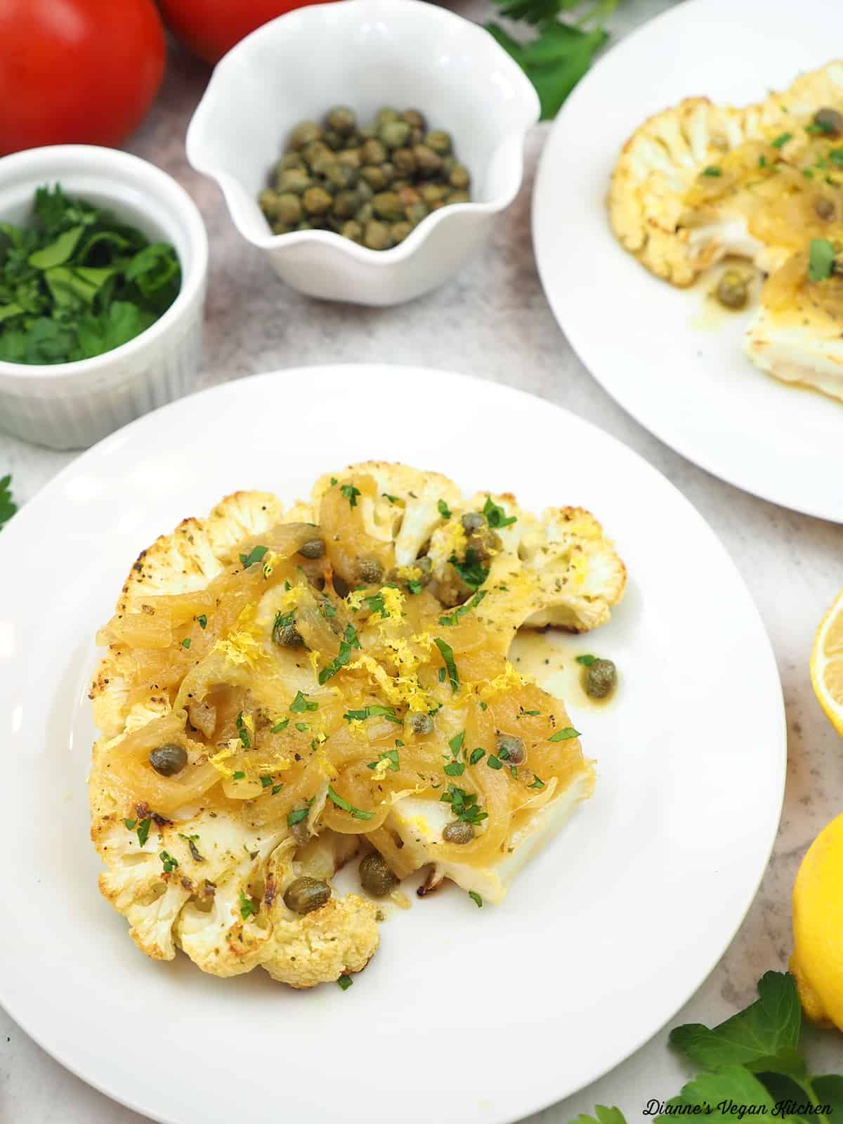 two plates of cauliflower with capers, lemon, parsley, and tomatoes