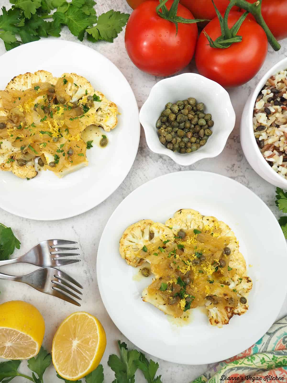 two plates of cauliflower cutlets with capers, lemon, rice, and tomatoes