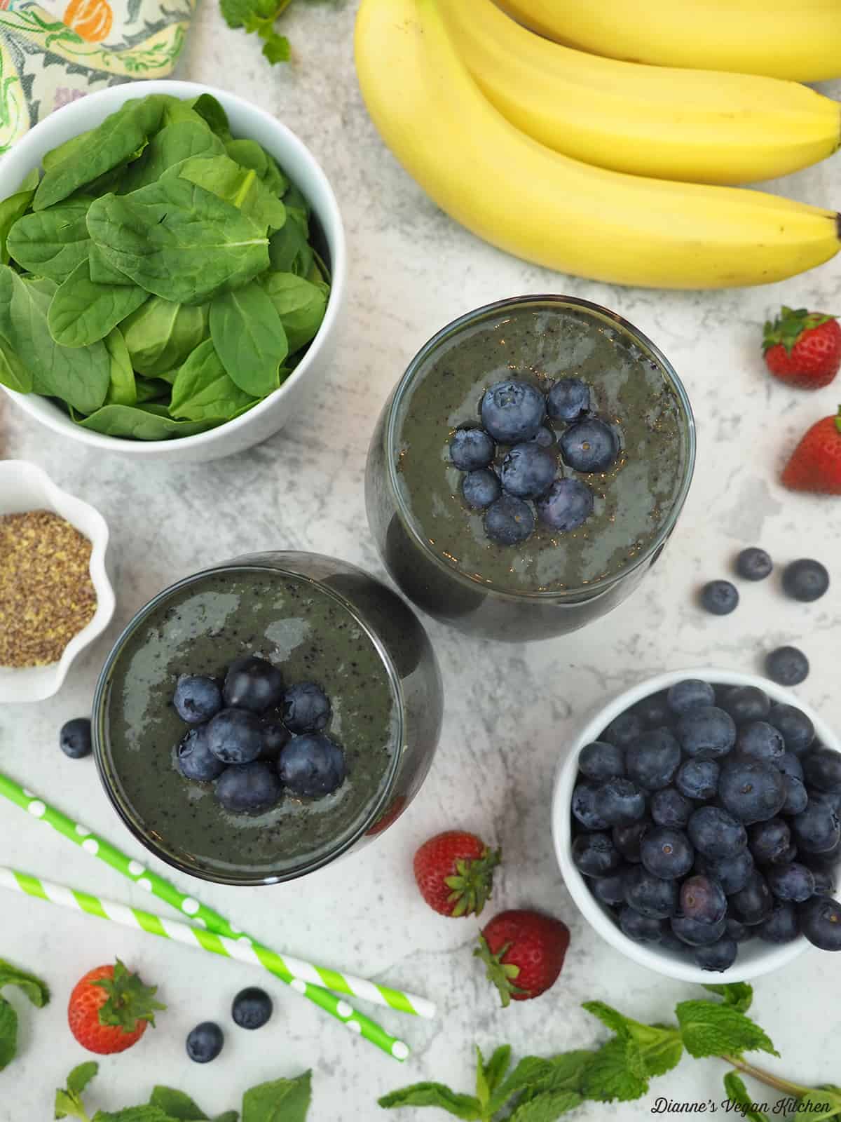 Overhead shot of smoothie with blueberries, bananas, strawberries and a bowl of spinach