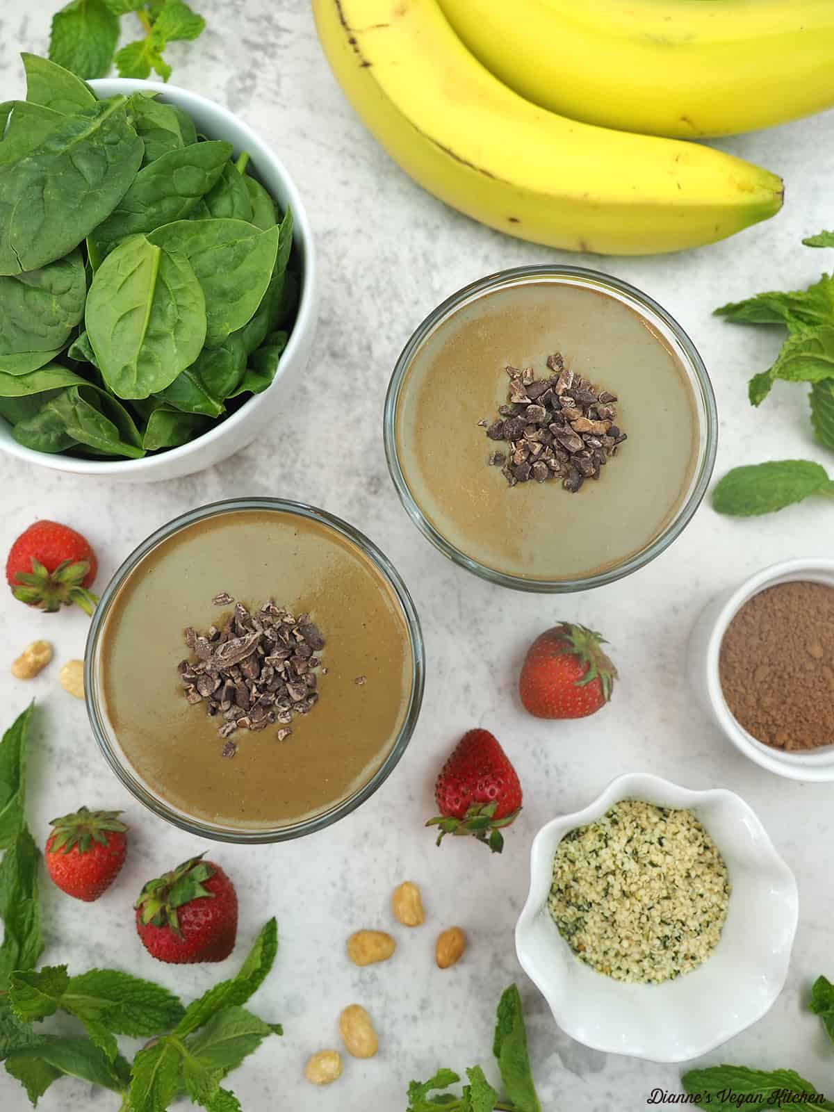 Top two smoothie glasses with banana, spinach and strawberries