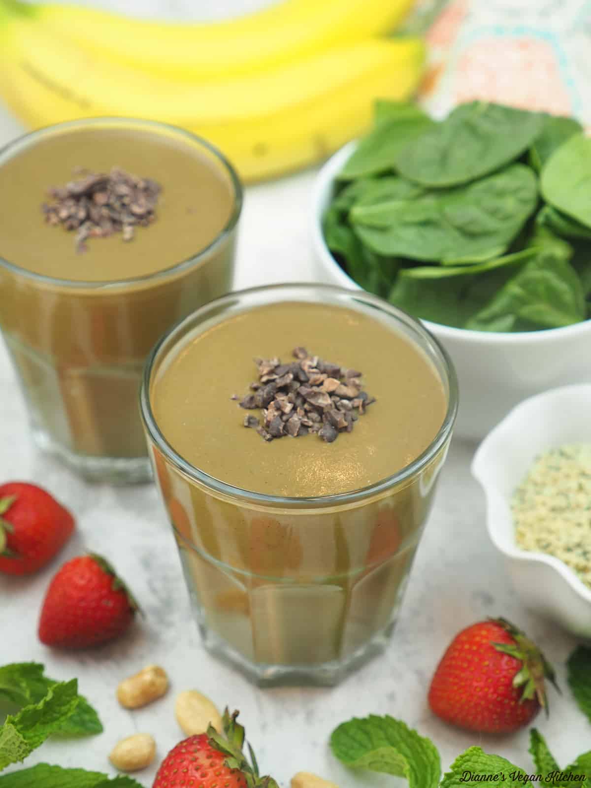 two glasses of smoothies with strawberries, bananas, and spinach