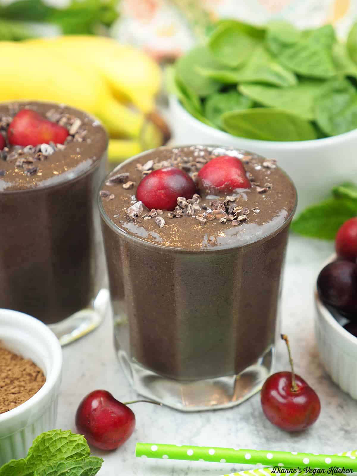 two glasses of smoothies with cacao, cherries, spinach, and bananas