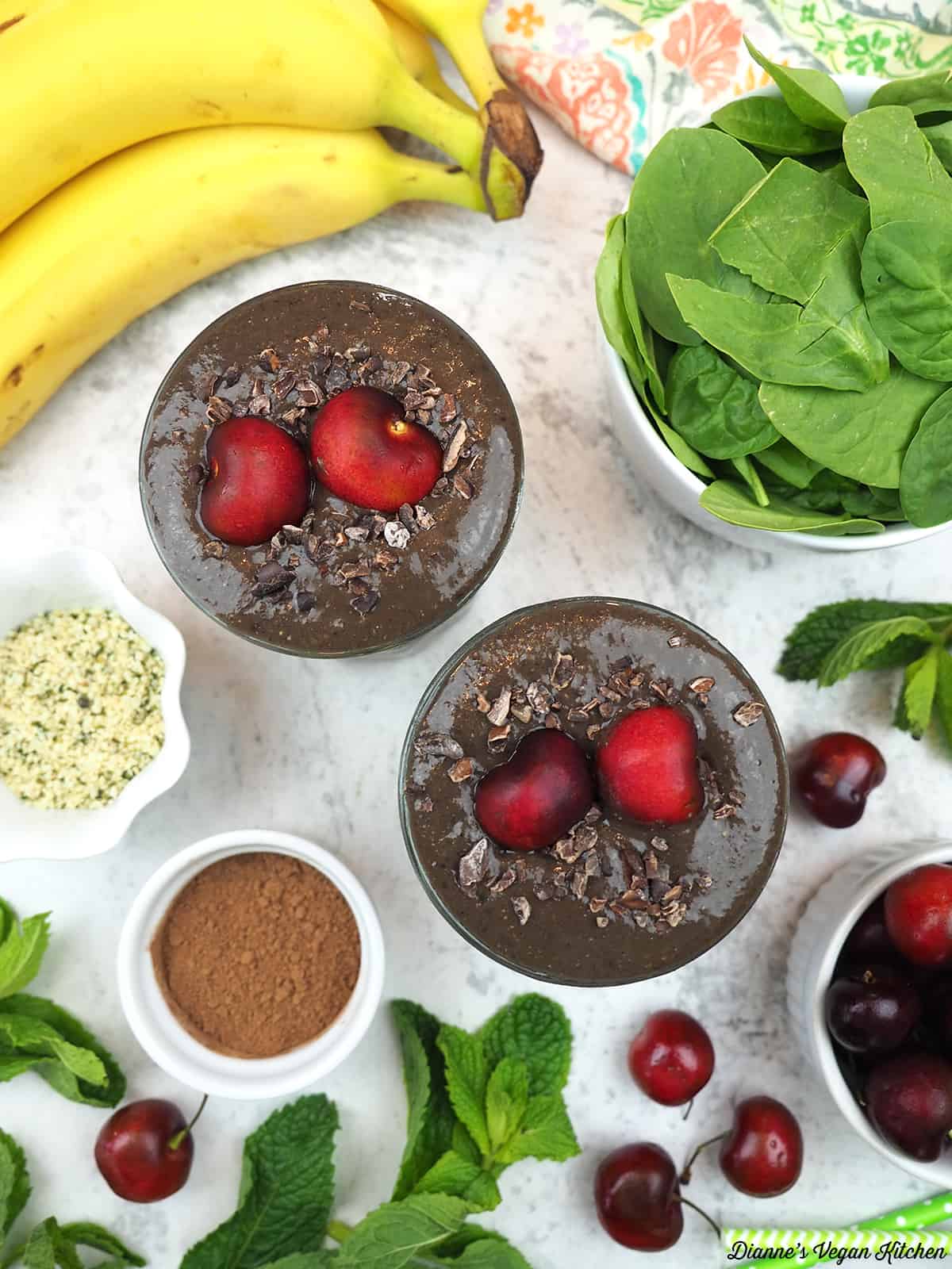 two glasses of smoothies overhead with bananas, spinach, cherries, hemp seeds, and cacao