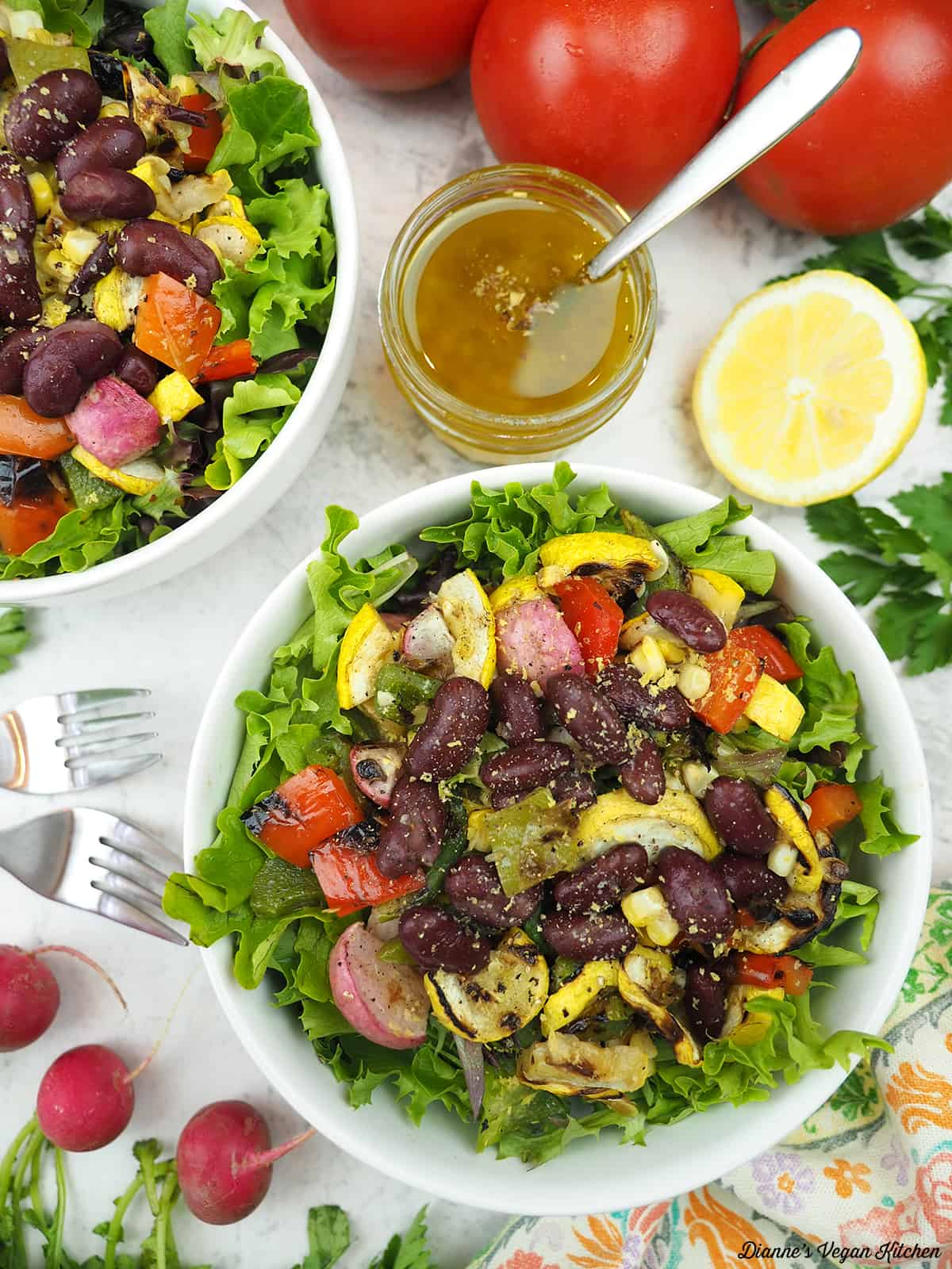 two bowls of salad overhead surrounded by dressing, lemons, tomatoes, and radishes