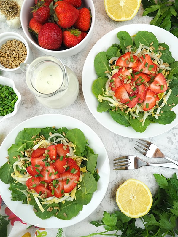two bowls of salad with strawberries, dressing, and lemon
